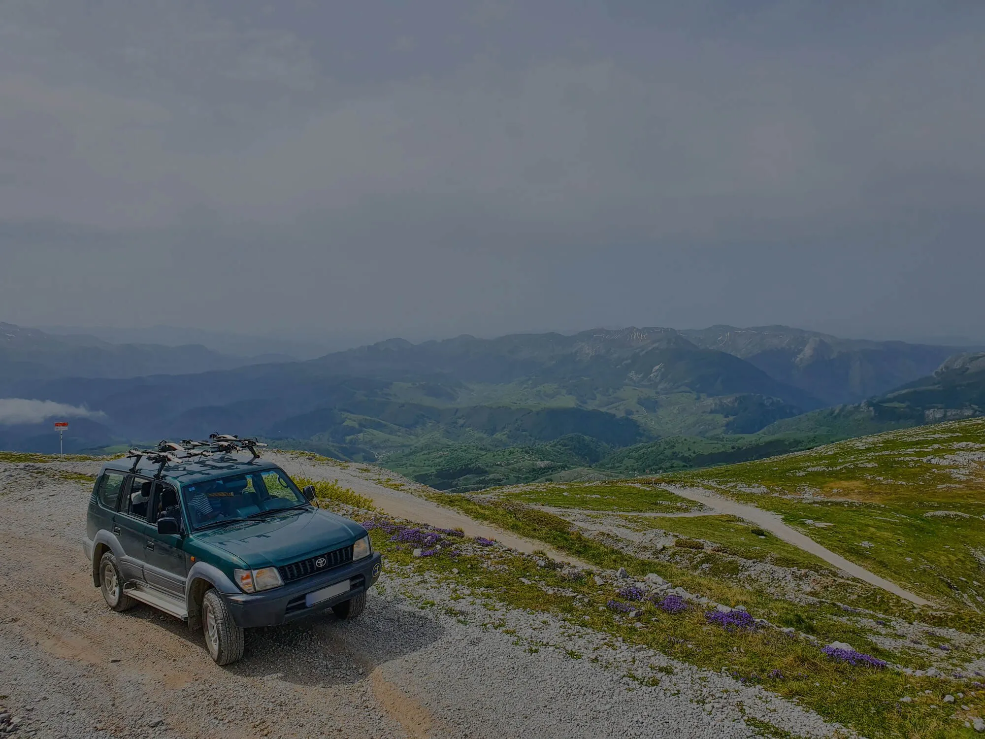 A green Toyota 4x4 on a gravel track high on Igman, under a dark sky